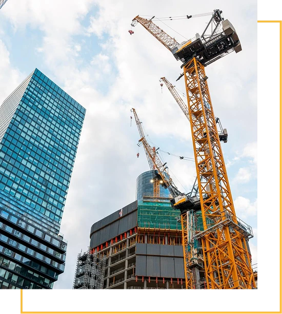 Several tall cranes are positioned above modern, partially constructed skyscrapers, with a glass building reflecting the sky on the left. The scene is set against a backdrop of scattered clouds.