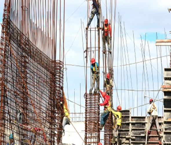 Construction workers wearing safety helmets and harnesses climb and work on tall steel rebar structures at a building site under a blue sky.
