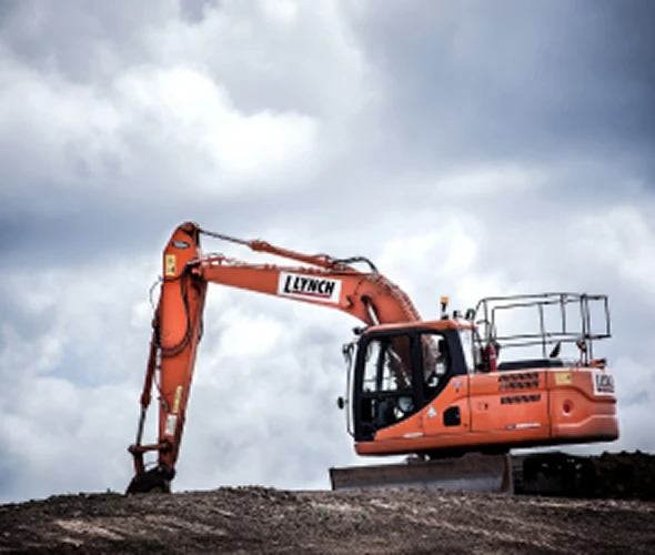 An orange excavator with the brand name "Lynch" on the arm is digging into a mound of dirt under a cloudy sky.
